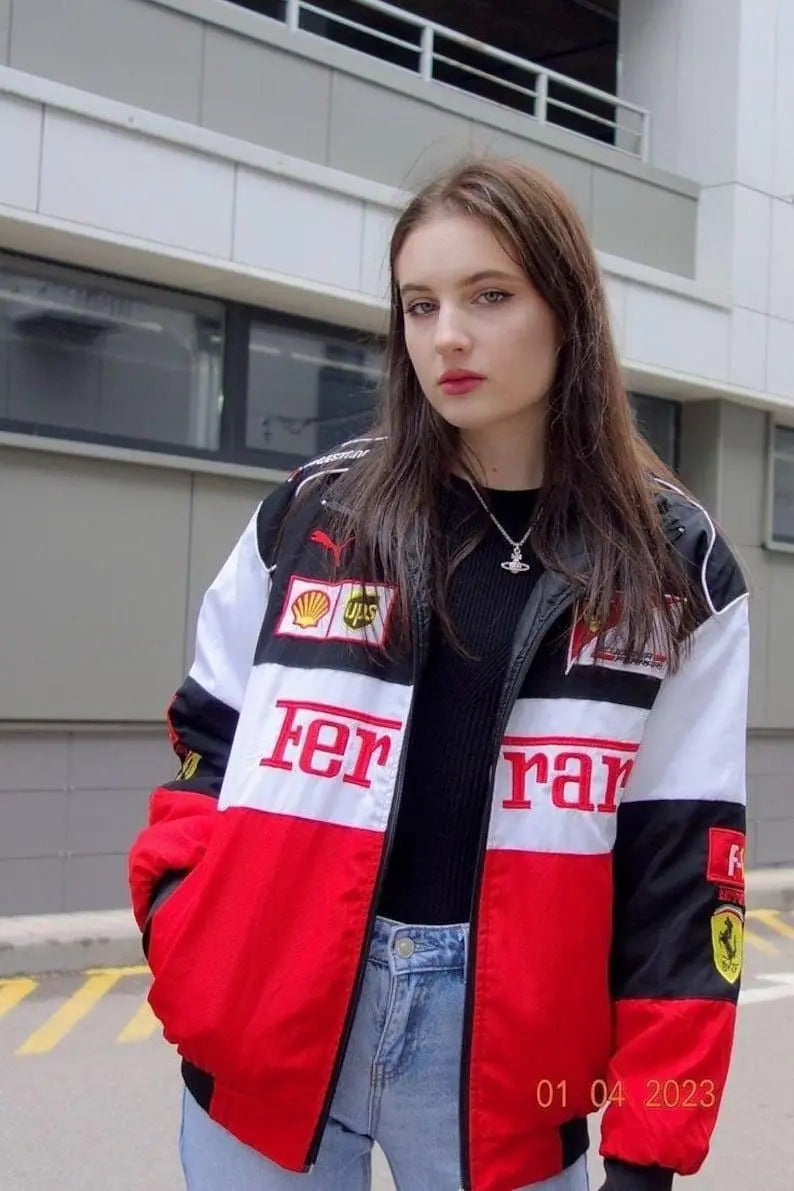 Young woman in streetwear style, wearing a red racing jacket, black top, and jeans outdoors.
