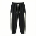 Black streetwear jogger pants with white side stripes and drawstring waist on white background