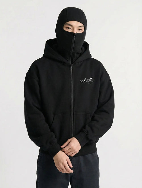 Man in black zip-up hoodie with face cover, minimalist streetwear style, white script logo