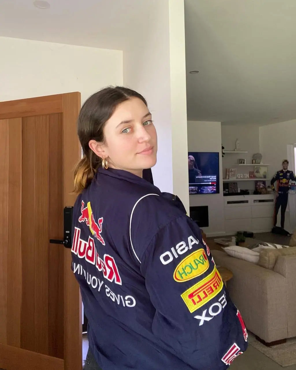 Woman wearing navy racing-inspired streetwear jacket with sponsor patches in a modern living room