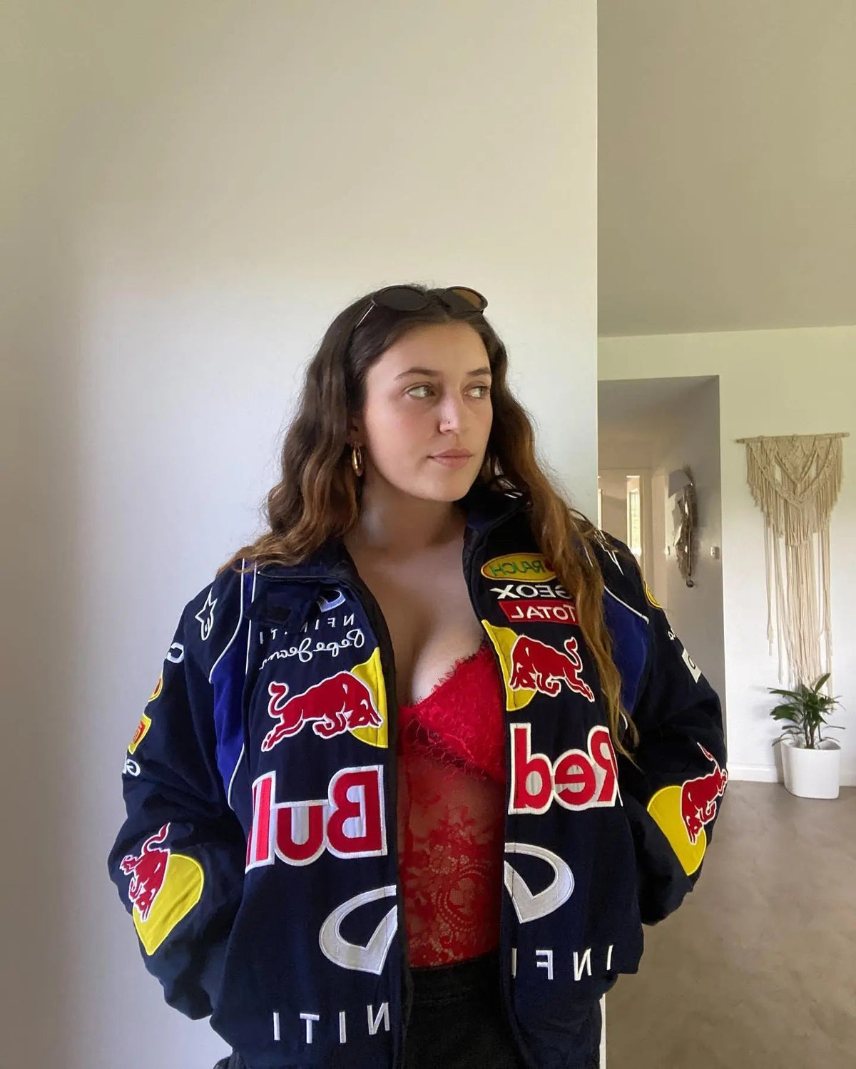 Woman wearing navy streetwear racing jacket with Red Bull logos and a red lace top indoors