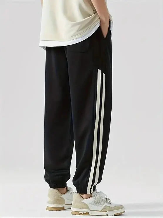 Black striped track pants with white side stripes, elastic cuffs, casual streetwear style.