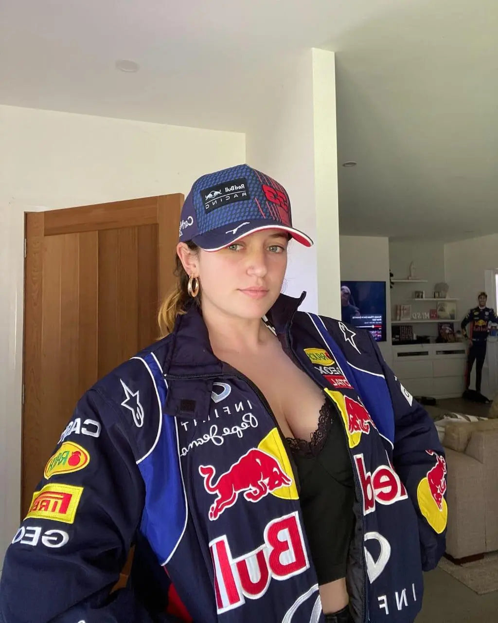 Woman in Red Bull Racing jacket and cap standing indoors, Gen Z streetwear fashion style.
