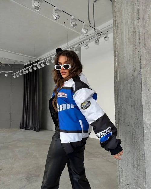 Woman wearing a blue and white colorblock streetwear jacket and black pants in a modern loft