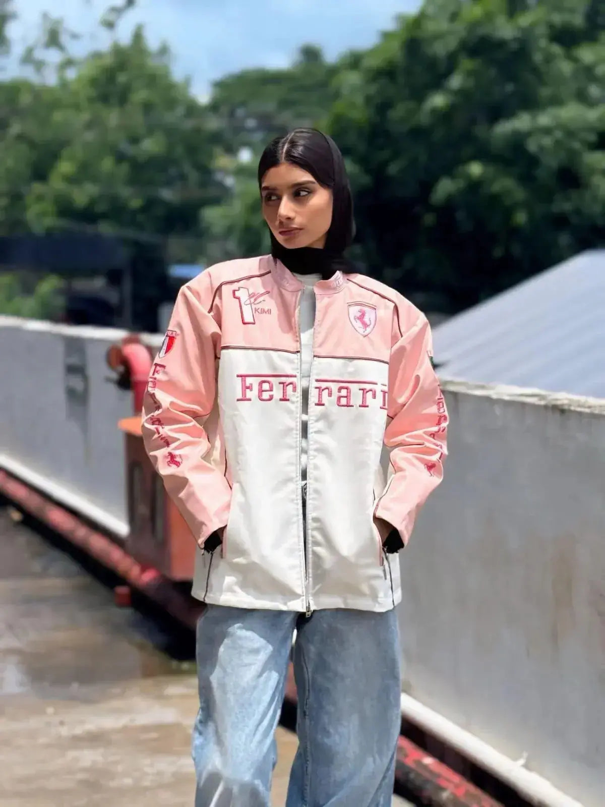Woman wearing light pink Ferrari racing jacket and blue jeans outdoors, modern streetwear style