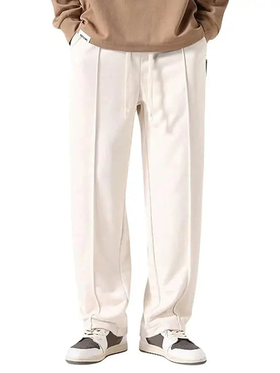 Beige straight-leg track pants with front seam detail, drawstring waist, and streetwear sneakers.