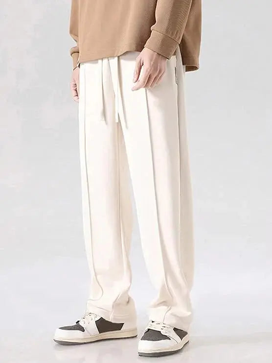 Cream streetwear track pants with drawstring waist and relaxed fit, styled with sneakers.