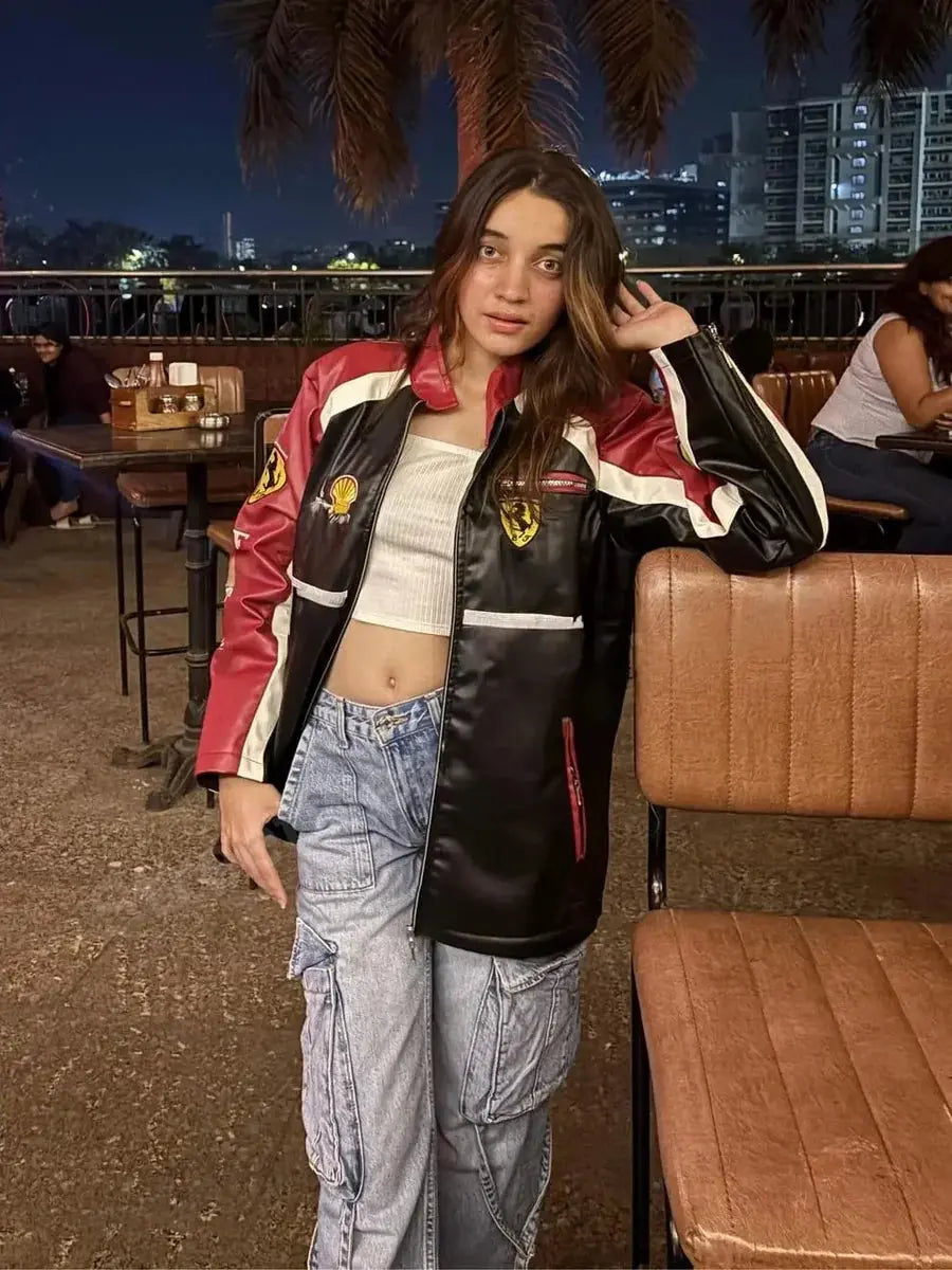 Woman in oversized red and black Ferrari jacket and cargo jeans, streetwear style at night cafe.